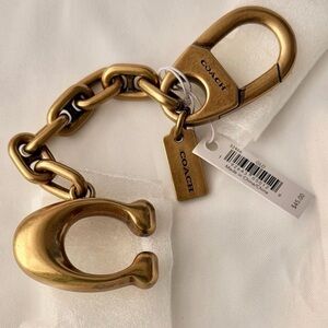 NWT Coach Signature bag charm in a gold-tone metal finish.